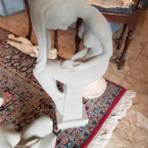 פסל עשוי חומר יצוק בגוון בטון אפור, בדמות נערה עירומה ארוכת שיער