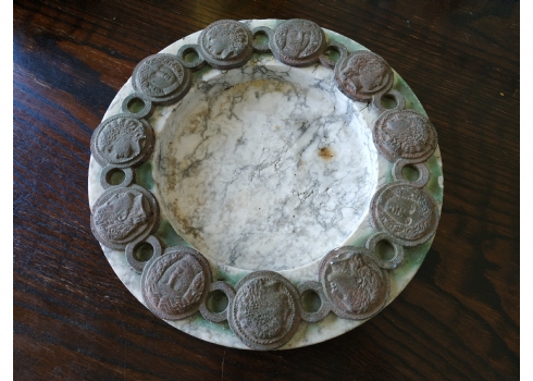 כלי עגול גדול ומאסיבי עשוי שיש, מעוטר בחלקו העליון מדליוני ברונזה