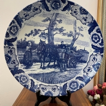 צלחת דלפט עגולה וגדולת מיימדים, עשויה חרסינה מעוטרת בהדפס כחול, חתומה