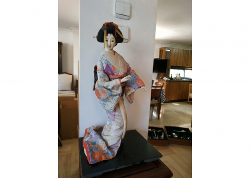 בובה יפנית גדולה לבושה בגד מסורתי טיקסי עשוי בד משי רקום, ניצבת על בסיס עץ שחור