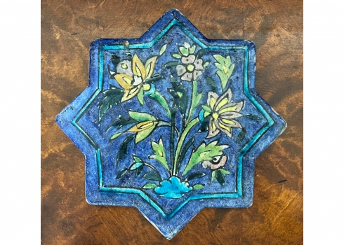אריח קרמיקה פרסי בעל צורה משוננת, מעוטר ציורי יד באמייל בדגם פרחים על רקע כחול