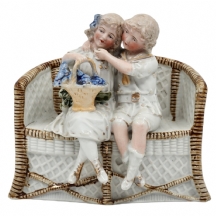 פסל ביסקוויט עתיק בדמות שני ילדים על ספסל קש, מעוטר בצביעת יד באמייל ובזהב