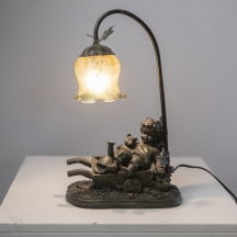 מנורה דקורטיבית בדמות ילד יושב על עגלת עץ קטנה לצד דובון צעצוע