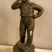 פסל ברונזה בדמות ילד ולצידו כד, עשוי פטינה חומה ובסיס שיש שחור מנומר