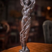 פסל ברונזה בדמות אישה מעורטלת פטינה חומה ובסיס שיש עגול שחור